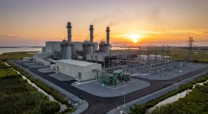 Aerial photograph of a combined-cycle natural gas power plant and electrical switchyard situated in a coastal wetland at sunset.